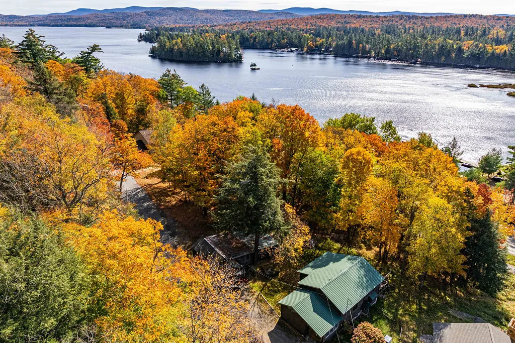 Aerial view of the green-roofed cabin among autumn trees with Raquette Lake and its islands behind it