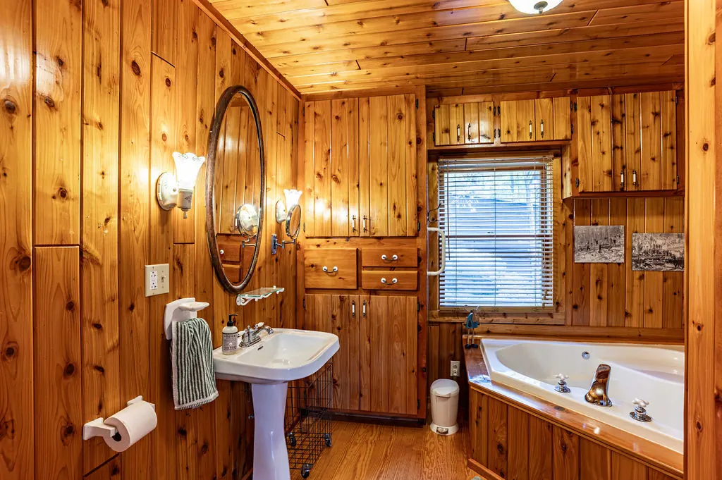 Knotty-pine bathroom with a pedestal sink, oval mirror and a corner jetted tub