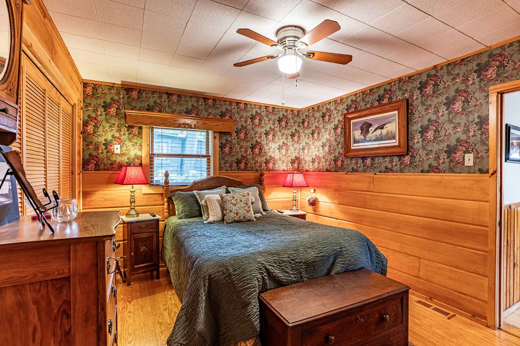 Bedroom with rose-patterned wallpaper, a queen bed with a green quilt, pine wainscoting and red lamps