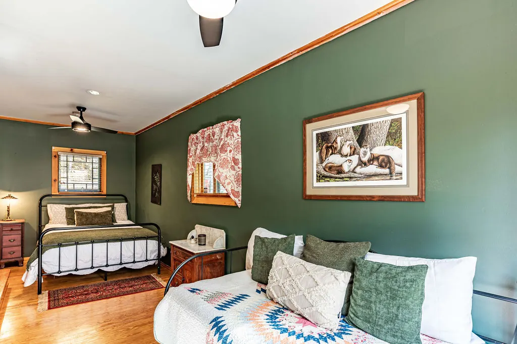 Green bedroom with a black iron bed, a white daybed and framed prints
