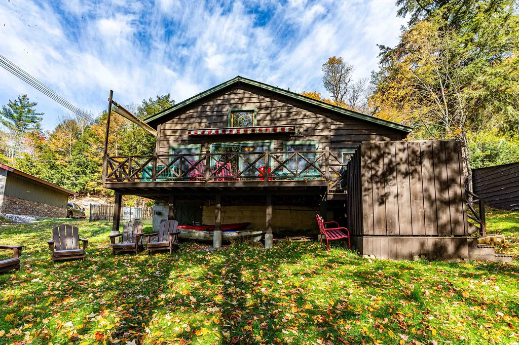 The back of the cabin with its raised deck, red rockers and Adirondack chairs on the lawn in autumn