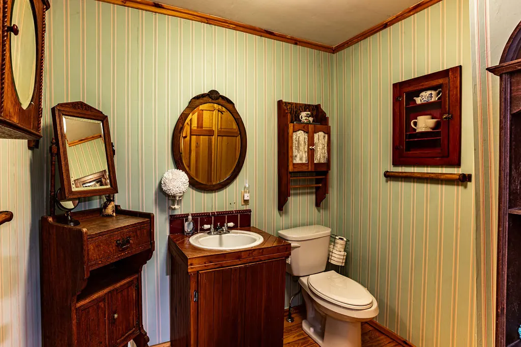 Half bathroom with striped wallpaper, a wooden vanity and antique mirrors